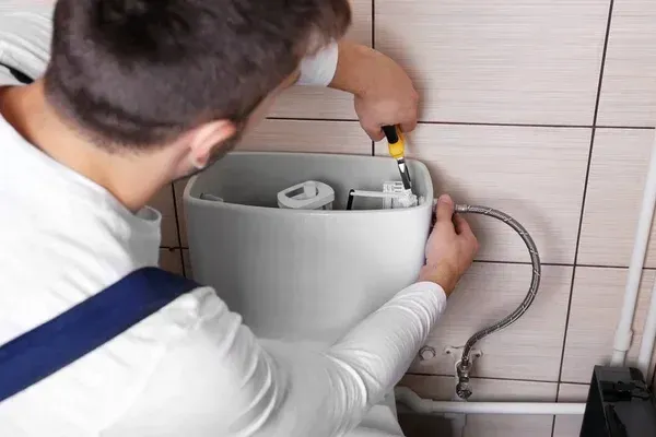 A plumber adjusting the fill valve inside an open toilet tank with a screwdriver