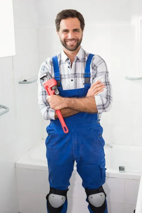 John Plumbing, founder of Green Country Plumbing, holding a pipe wrench in a tiled bathroom